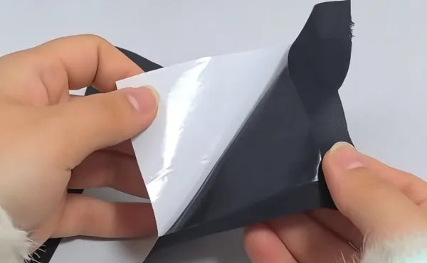 Peeling off the white release paper to expose the hot-melt adhesive layer on fabric